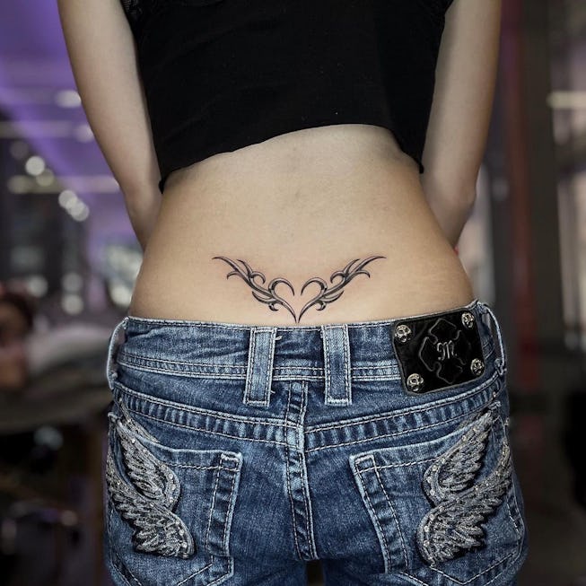 Delicate tribal flourishes bloom across the lower back in this elegantly symmetrical design, creating a stunning focal point that perfectly complements the natural curves of the body. The flowing linework forms an almost butterfly-like pattern with ornate scrollwork that feels both timeless and feminine ✨ Positioned just above low-rise denim, this piece demonstrates how strategic tattoo placement can create beautiful visual harmony with your personal style.